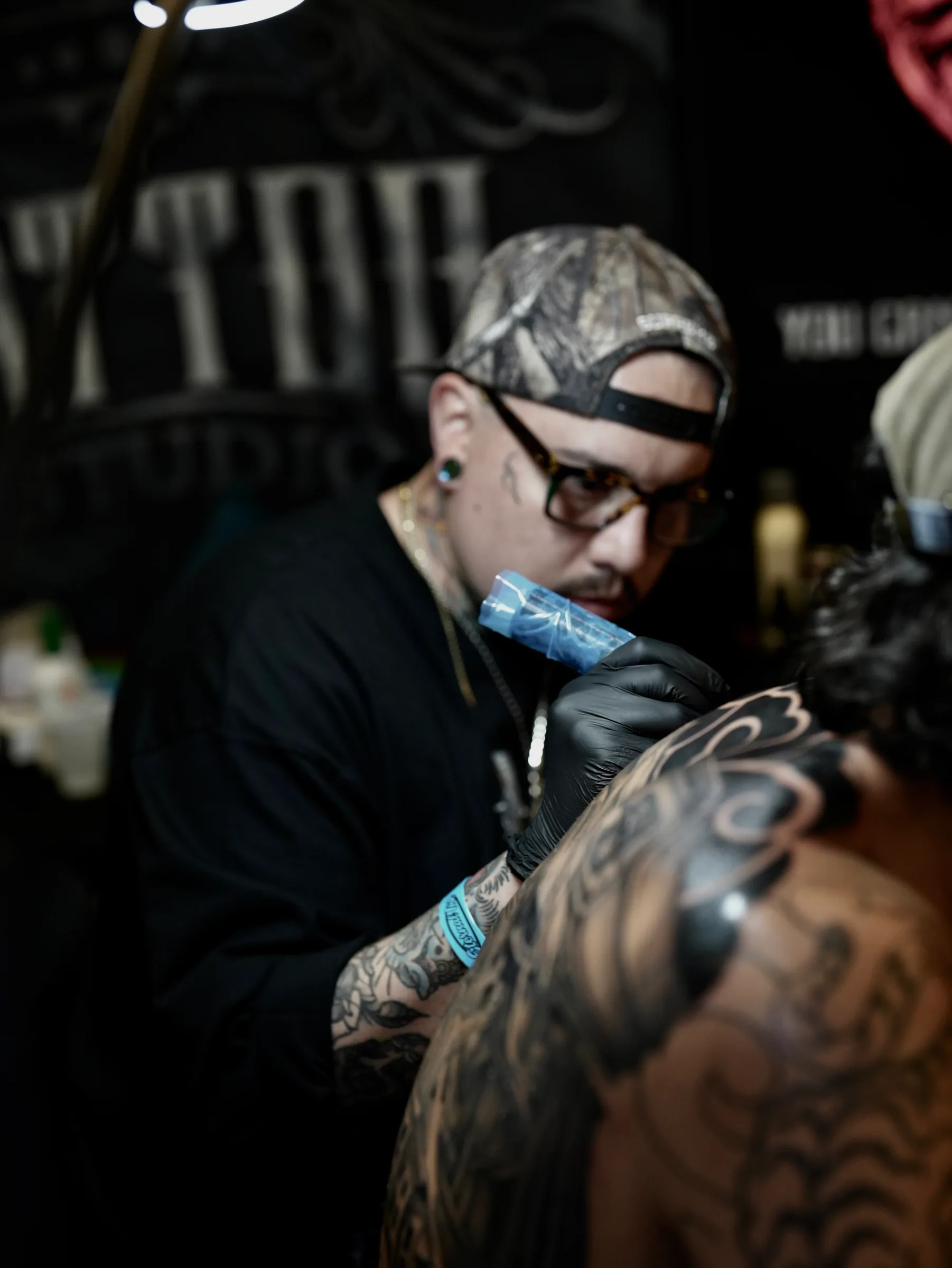 Ansias tattooing, close over a client's shoulder, low warm light